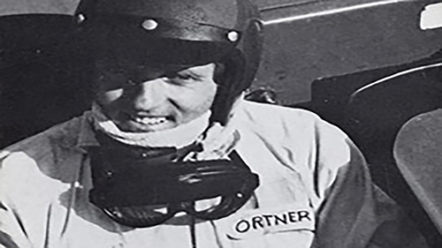 Schwarz-Weiß-Aufnahme: Johannes Ortner mit Rennhelm und Brille im Cockpit, auf dem Overall der Schriftzug Ortner