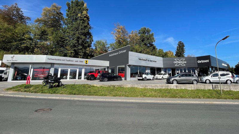 Das Autohaus Ortner in der Piccostraße 42 in Villach von der Straße aus: flacher Bau mit den Schriftzügen Autohaus Ortner, Verkauf und Service sowie Ortner 4x4, davor Fahrzeuge