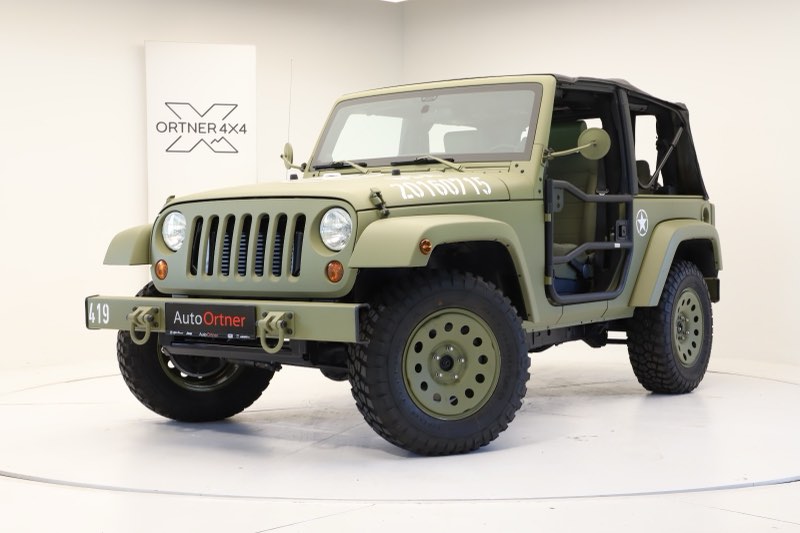 Ein olivgrüner Jeep Wrangler im Militärlook mit Sternemblem, Stahlfelgen und Geländebereifung vor der Wand mit dem Ortner-4x4-Zeichen