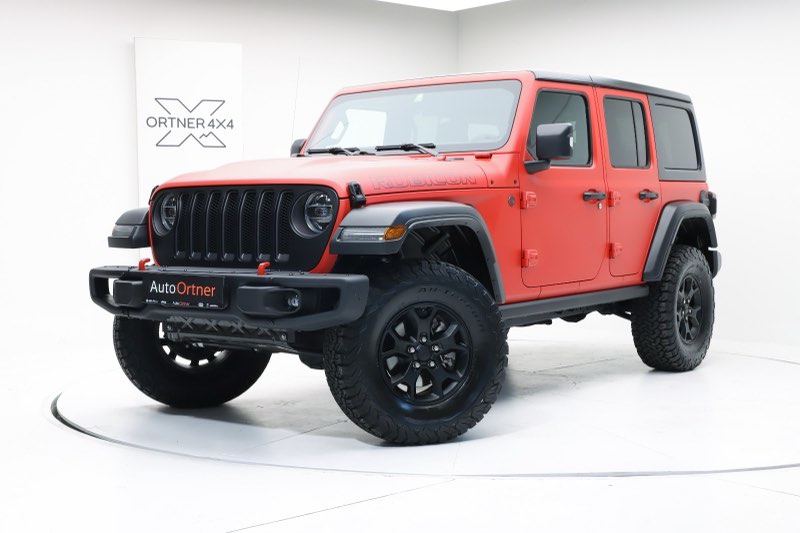 Ein roter Jeep Wrangler Rubicon Unlimited mit schwarzen Rädern und Geländebereifung vor der Wand mit dem Ortner-4x4-Zeichen