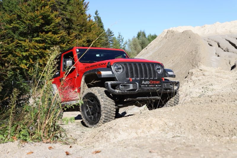 Ein roter Jeep Wrangler Rubicon mit Ortner-Kennzeichenhalter steht an einer steilen Schotterböschung in einer Schottergrube